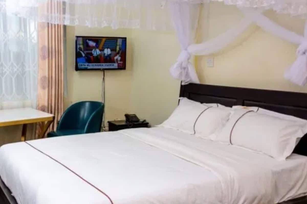 Quarto de hotel com uma cama, uma escrivaninha, uma cadeira, uma televisão e cortinas.