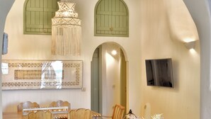A cozy living room with a sofa, coffee table, and chairs, an arched doorway, and a hanging light fixture. - Archon Villa by K&K (Oia)