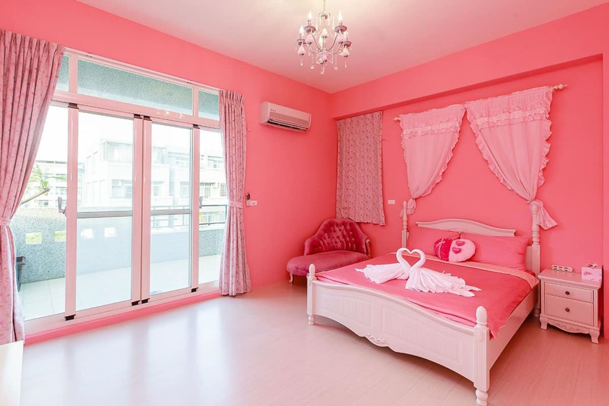 A pink-themed bedroom with a bed, curtains, a chandelier, and a nightstand.