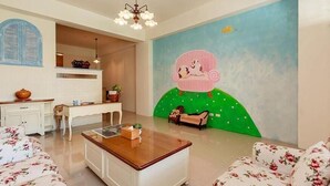 Una sala de estar con una mesa de centro de madera, un sofá floral y un sofá verde con un mural de una silla rosa y un perro.