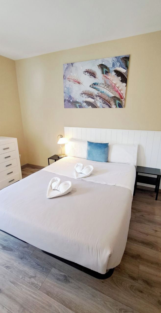 Hotelkamer met een groot bed, nachtkastje met lamp, dressoir en een schilderij aan de muur.