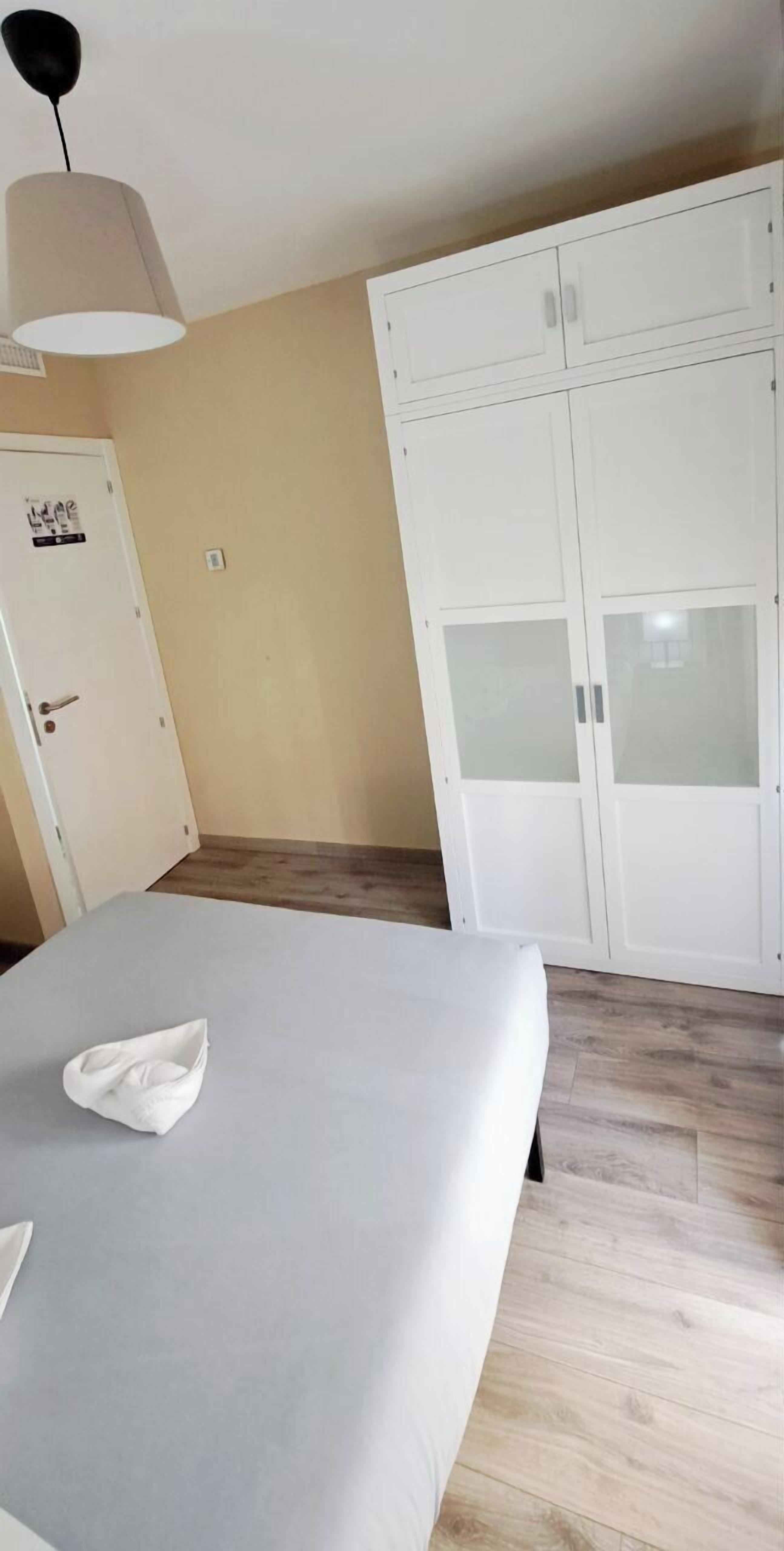 A bedroom with a bed, a wardrobe, and a ceiling lamp.