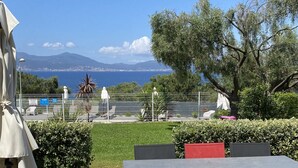 An outdoor seating area with tables and chairs, a view of the sea, and a distant mountain range.
