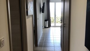 A hallway with a tiled floor, a flat-screen TV mounted on the wall, and a sliding glass door leading to a balcony.