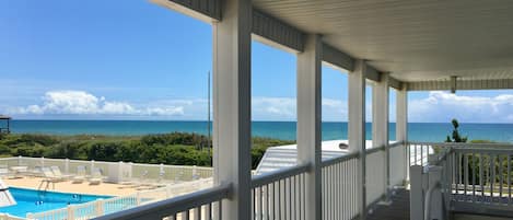Una terraza techada con piscina y sillas de descanso, con vista a una playa y al océano.