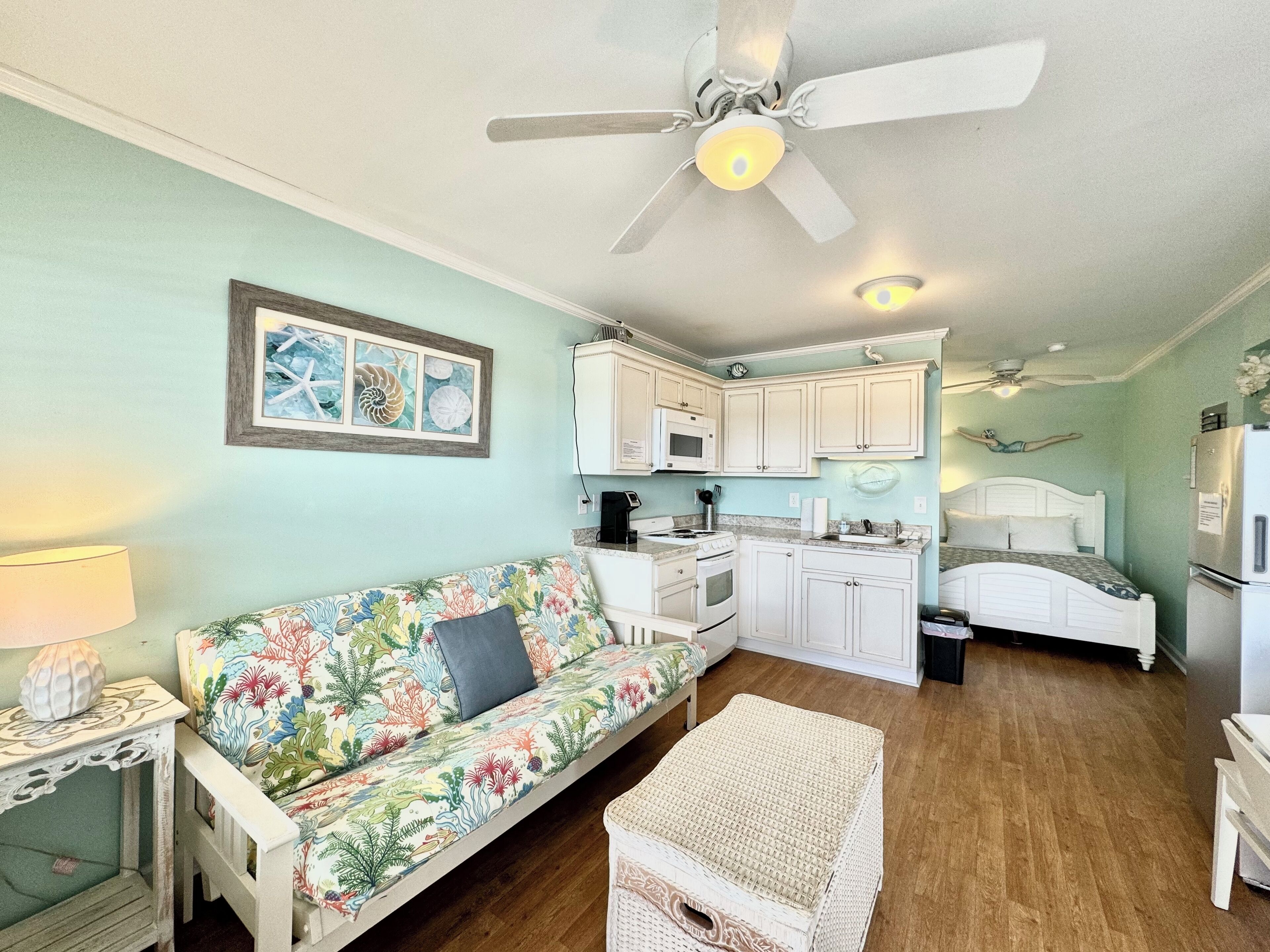 A compact living space with a kitchenette, a sofa, a bed, and a ceiling fan.