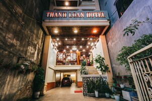 La entrada del Hotel Thanh Loan, con un coche estacionado adelante, plantas en macetas y una escalera que lleva al nivel superior.