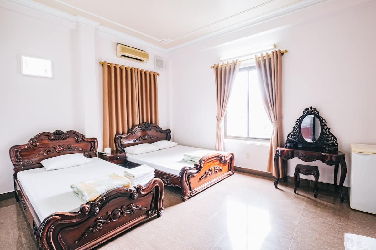 A room with two wooden beds, a small table, a mirror, and a window with curtains.