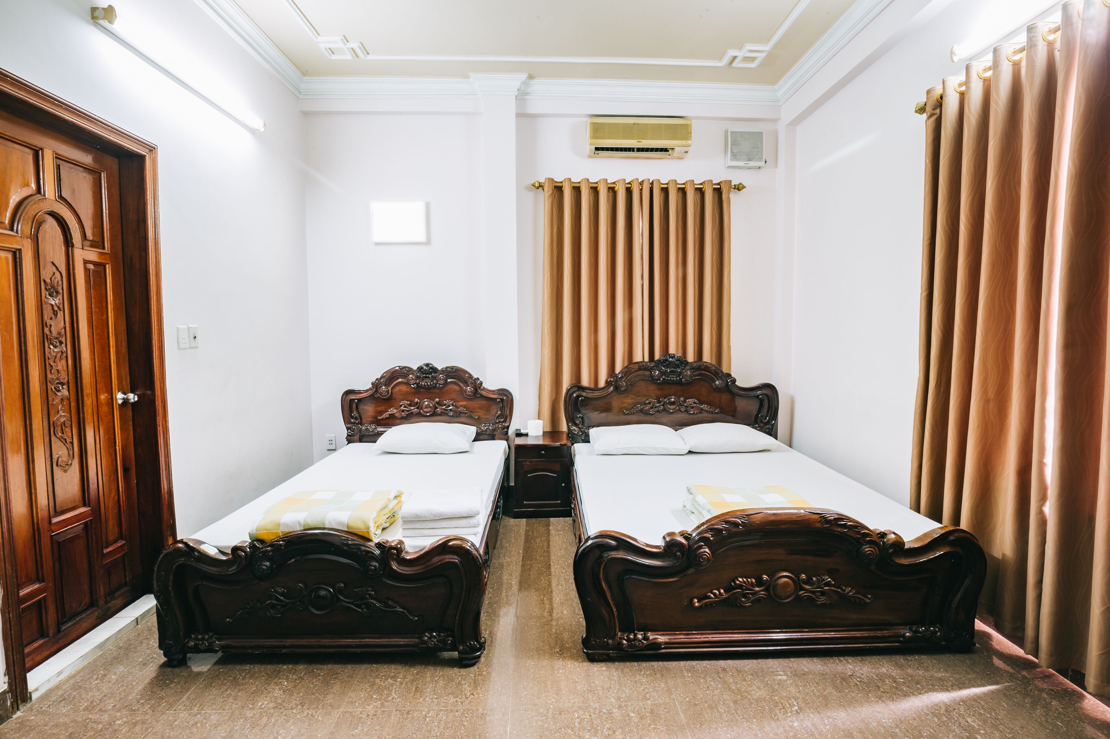 Une chambre d’hôtel avec deux lits en bois, une armoire et un luminaire au plafond.