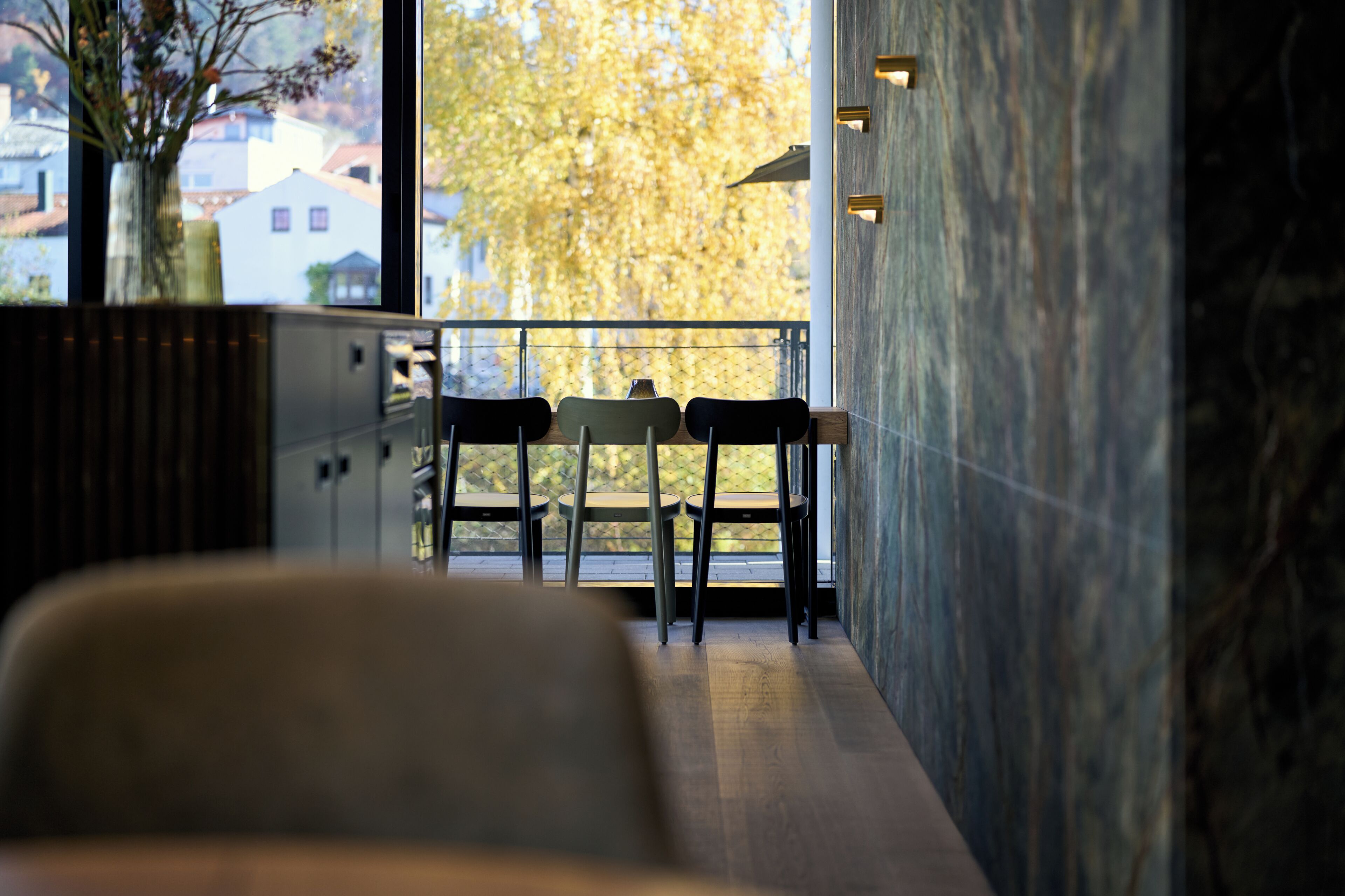 A modern interior with a seating area, a view of autumn trees, and a marble wall.