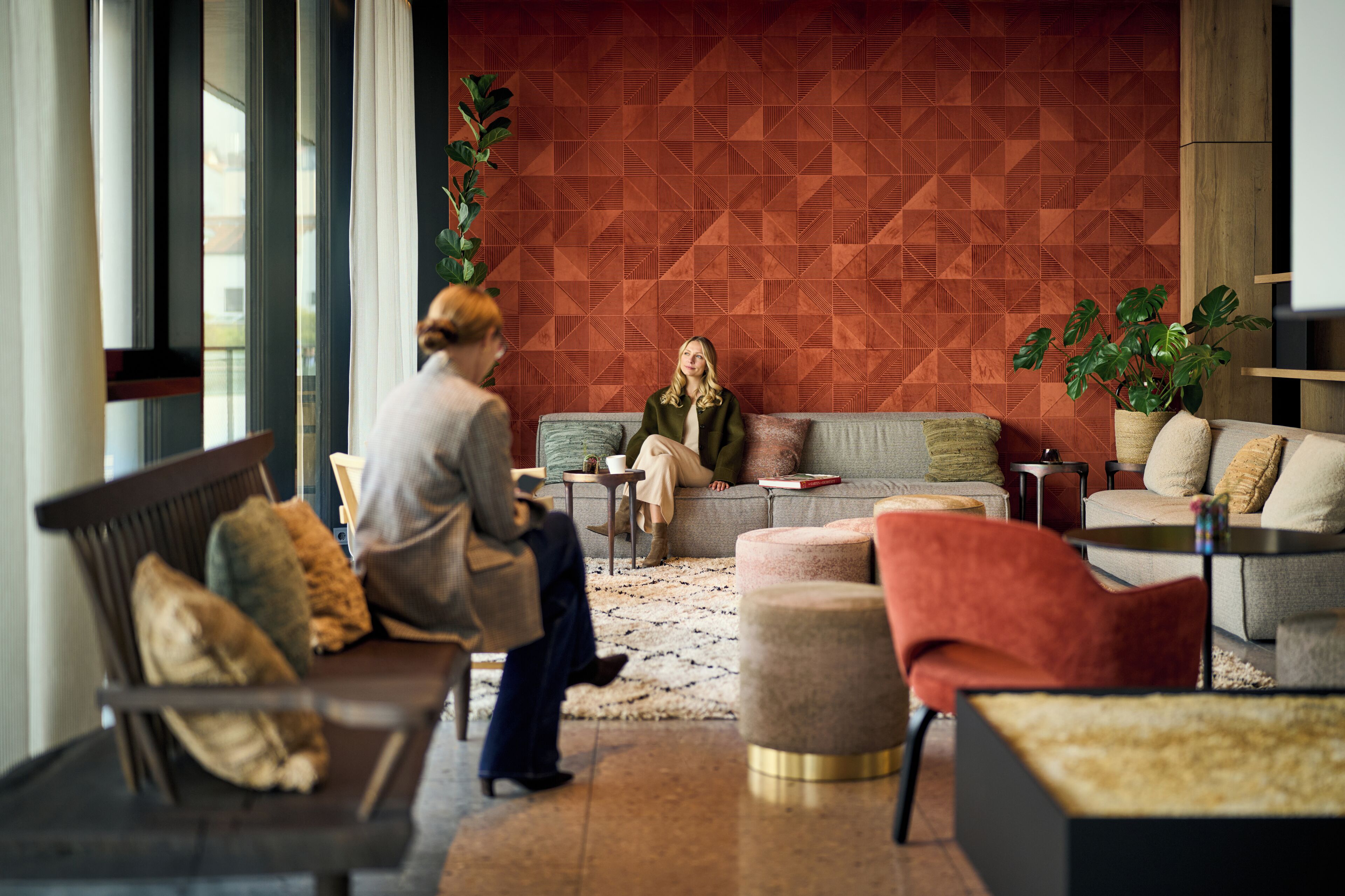 A modern lounge area with a geometric patterned wall, comfortable seating, and a potted plant.
