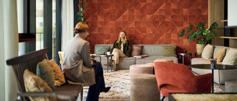 A modern lounge area with a geometric patterned wall, comfortable seating, and a potted plant.