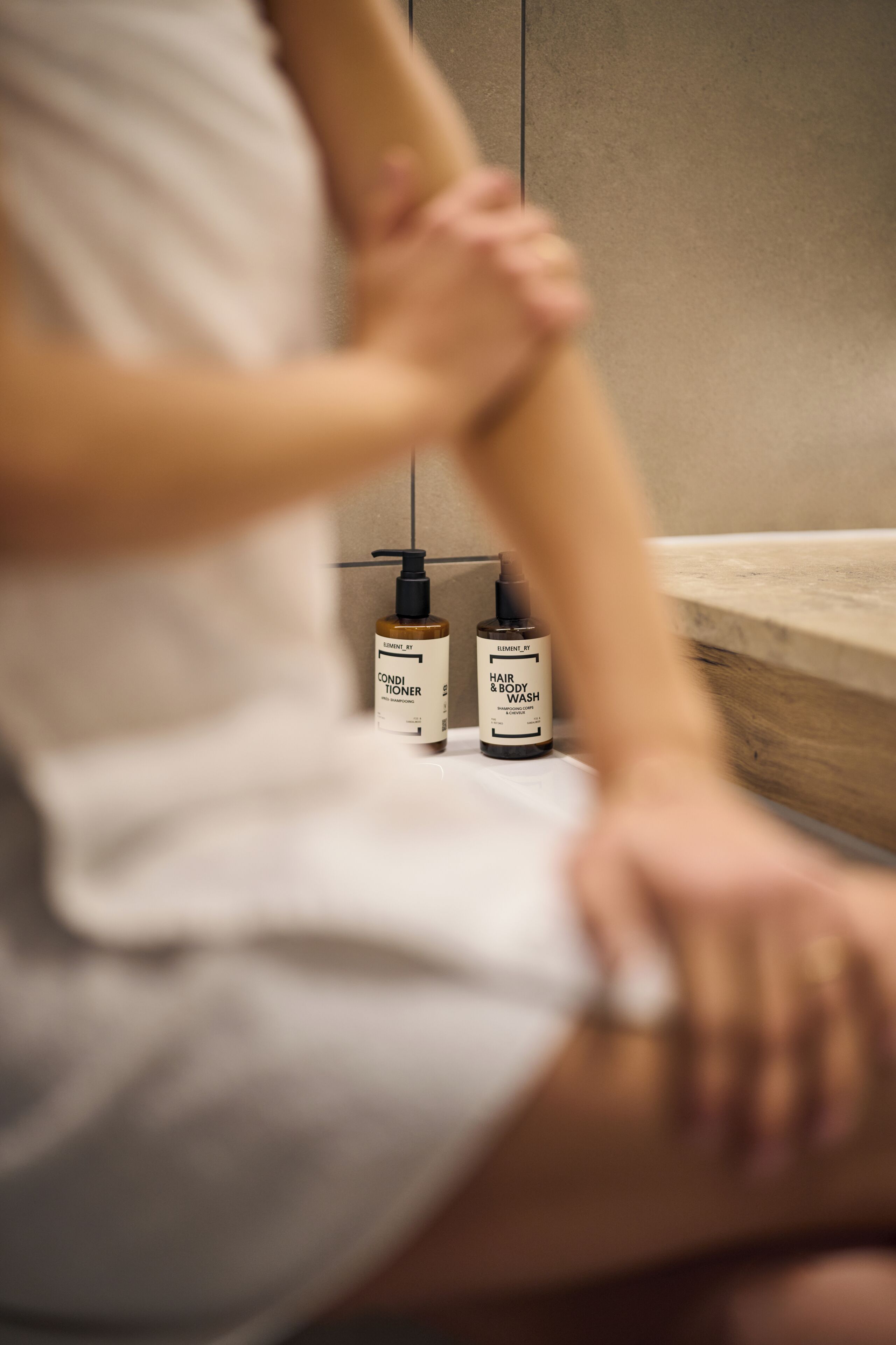 Une salle de bain avec une baignoire en bois, une serviette blanche et deux flacons de gel douche et de shampoing.
