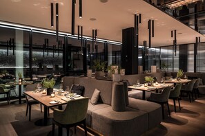Un ristorante moderno con tavoli alti, sedute imbottite e lampadari a sospensione.