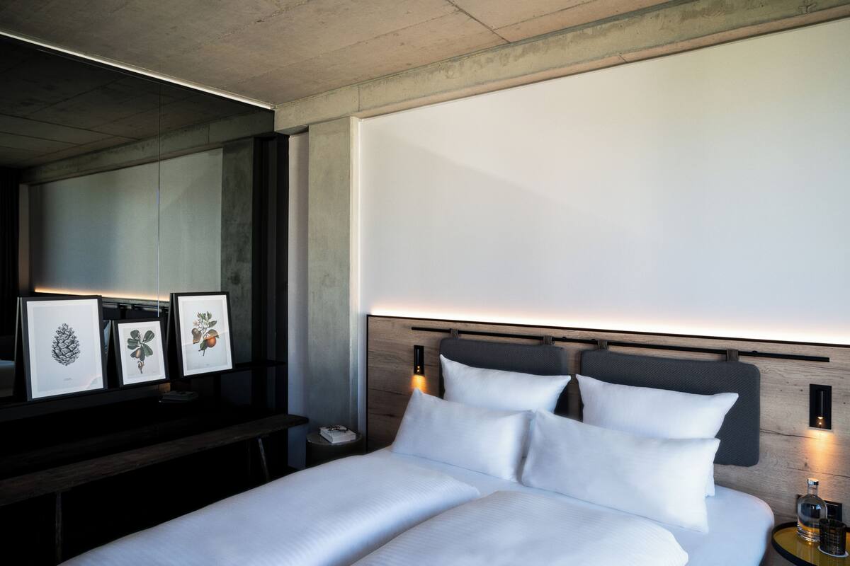 Ein modernes Hotelzimmer mit einem großen Bett, einem Nachttisch mit Lampe und gerahmten Pflanzenbildern an der Wand.