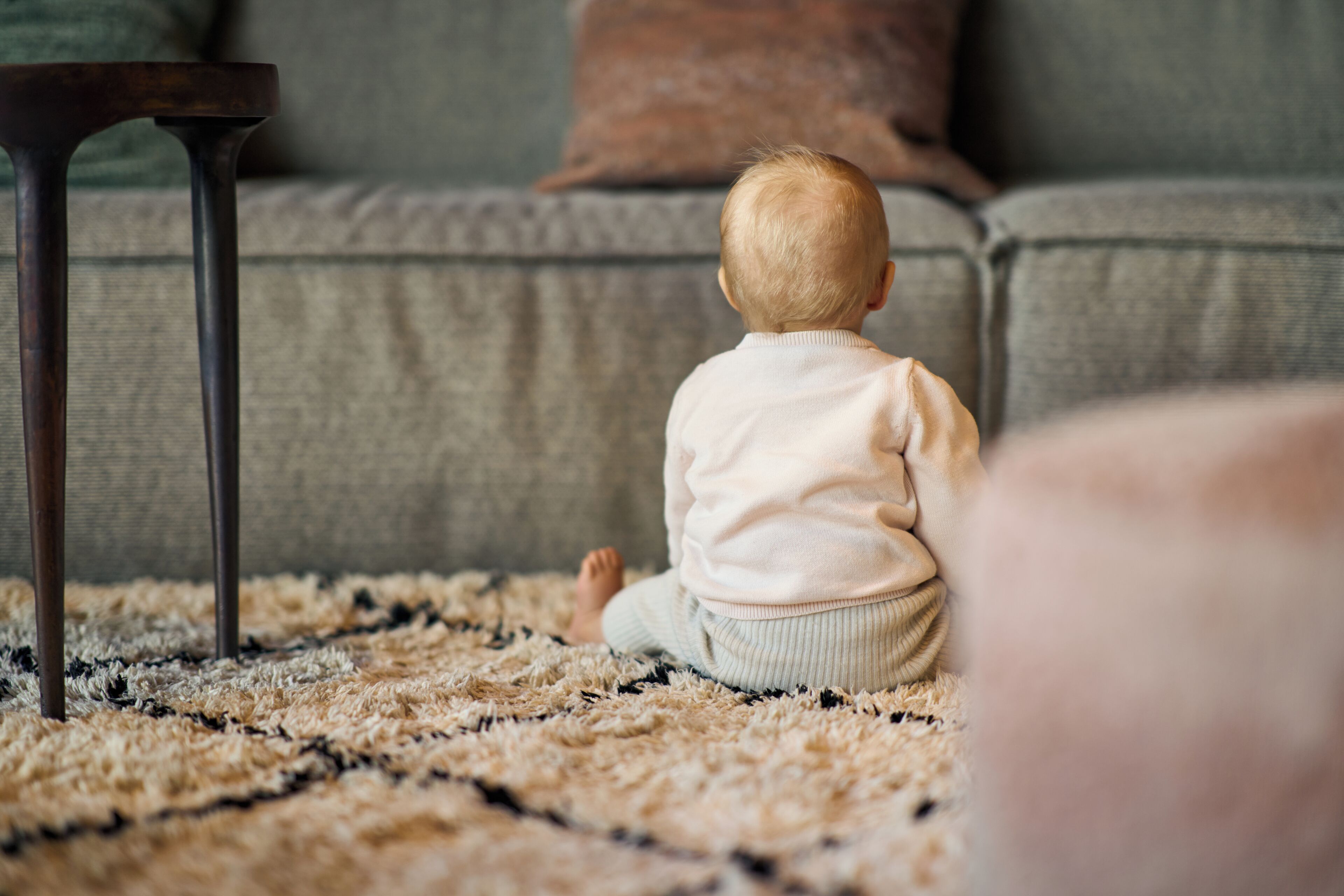 Un enfant est assis sur un tapis à motifs dans une pièce où se trouvent un canapé et une petite table.