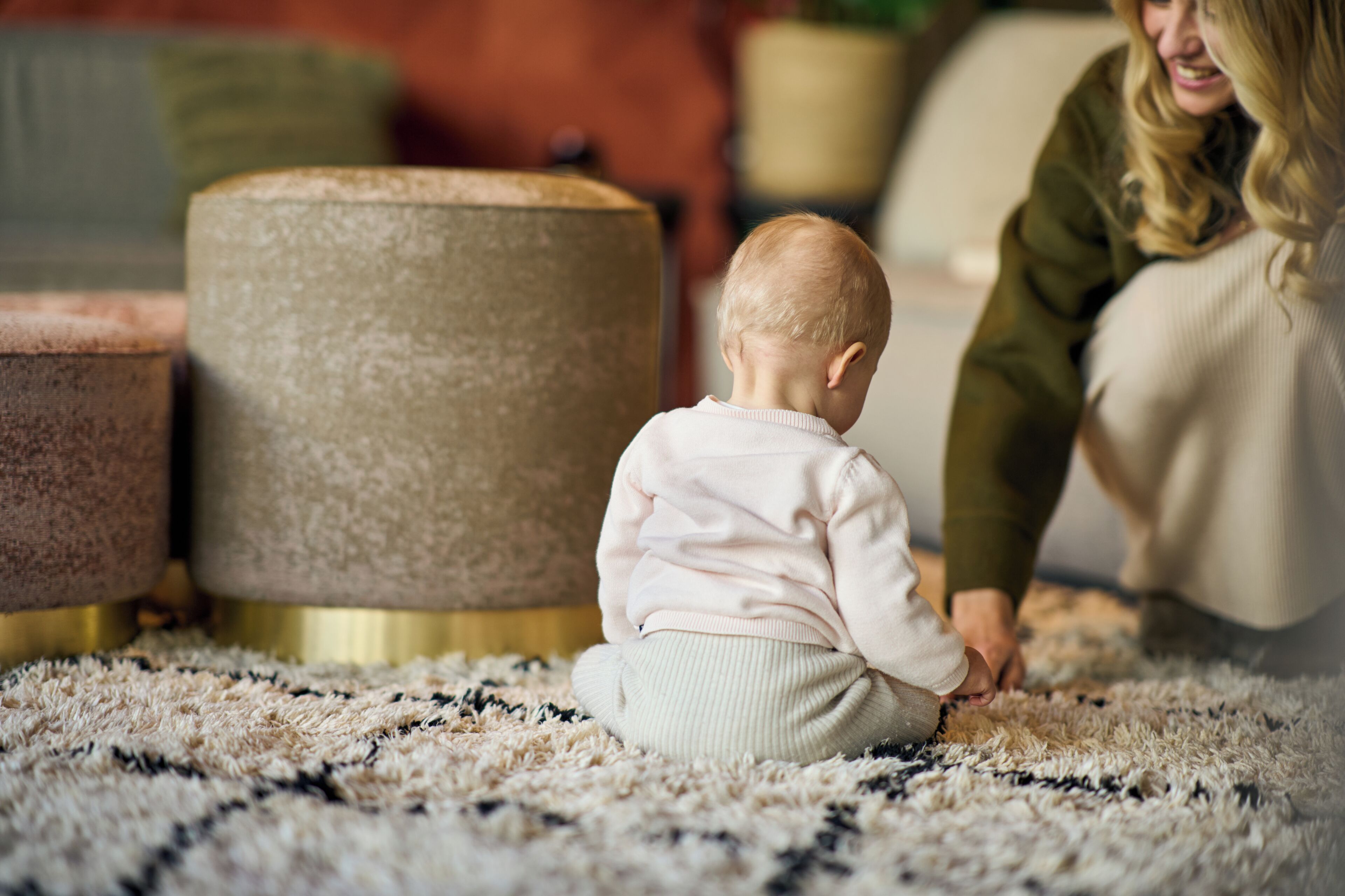 A child sitting on a patterned rug in a room with a large ottoman and a sofa.