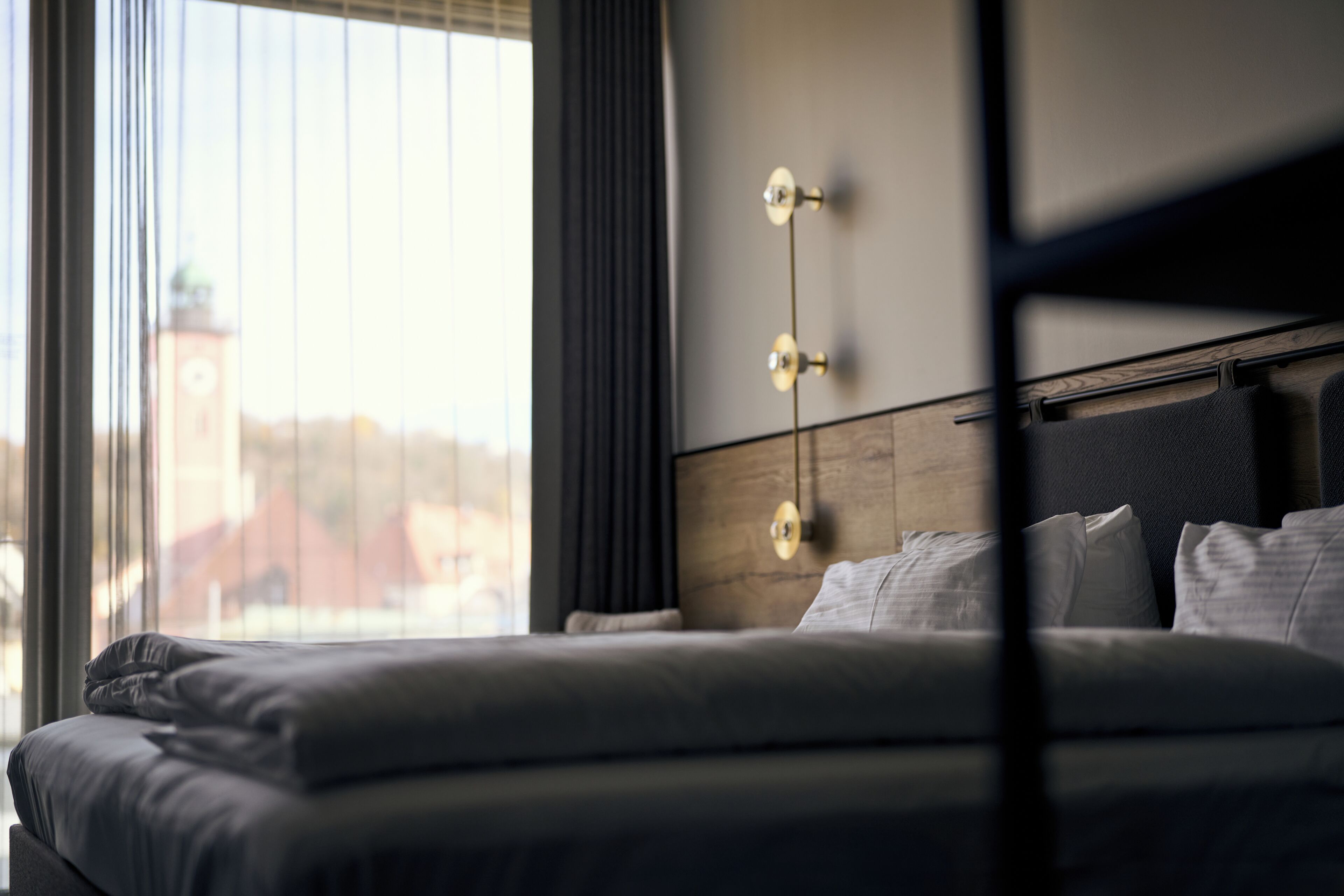 A hotel room with a bed, a window with blinds, and a view of a clock tower.