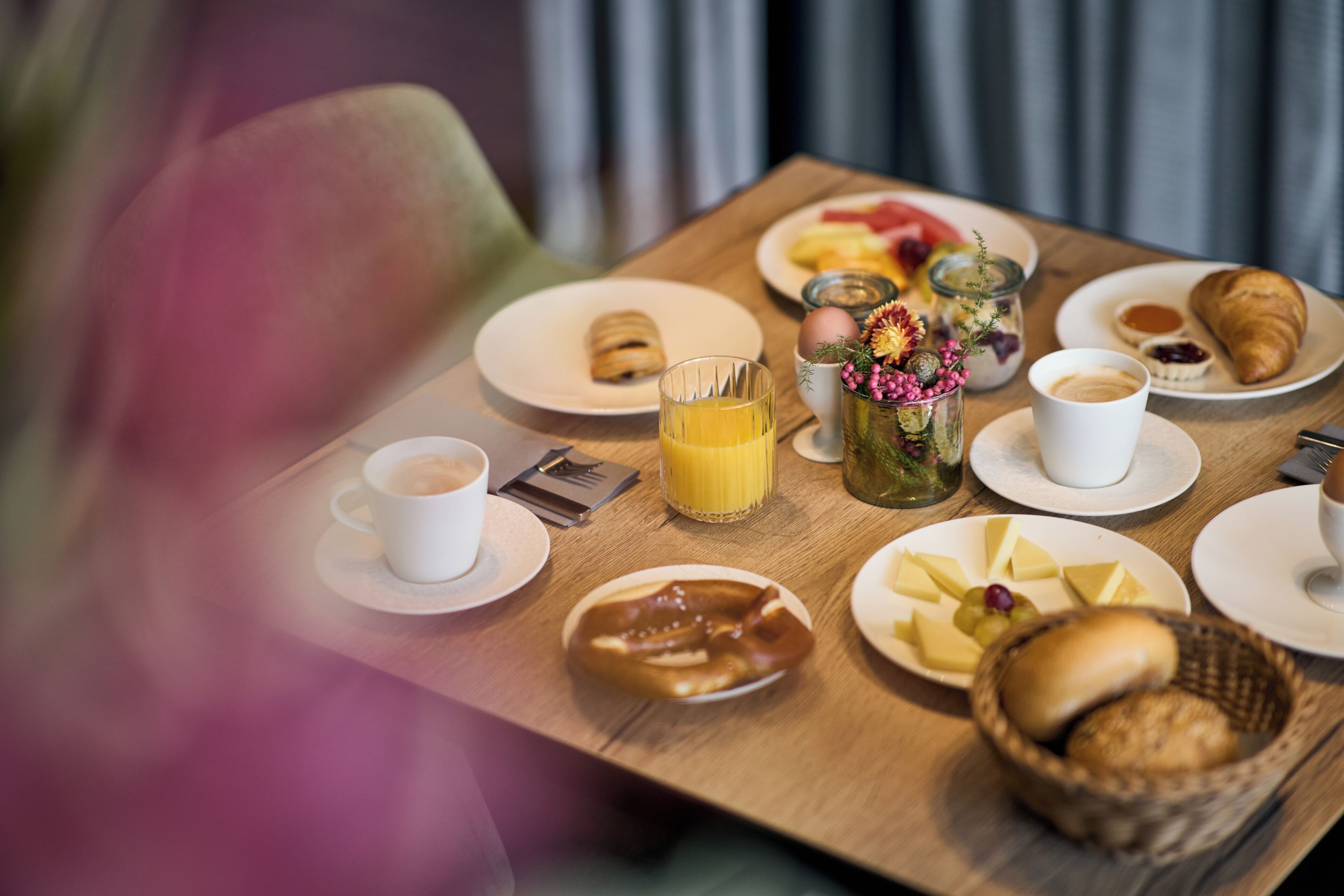 Una mesa de desayuno con platos de comida, un vaso de jugo de naranja, una taza de café y una cesta de pan.