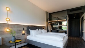 A modern bedroom with a large bed, bedside tables, a wall-mounted light fixture, and a view into the adjacent room. - Das Altmühltal (Eichstaett)