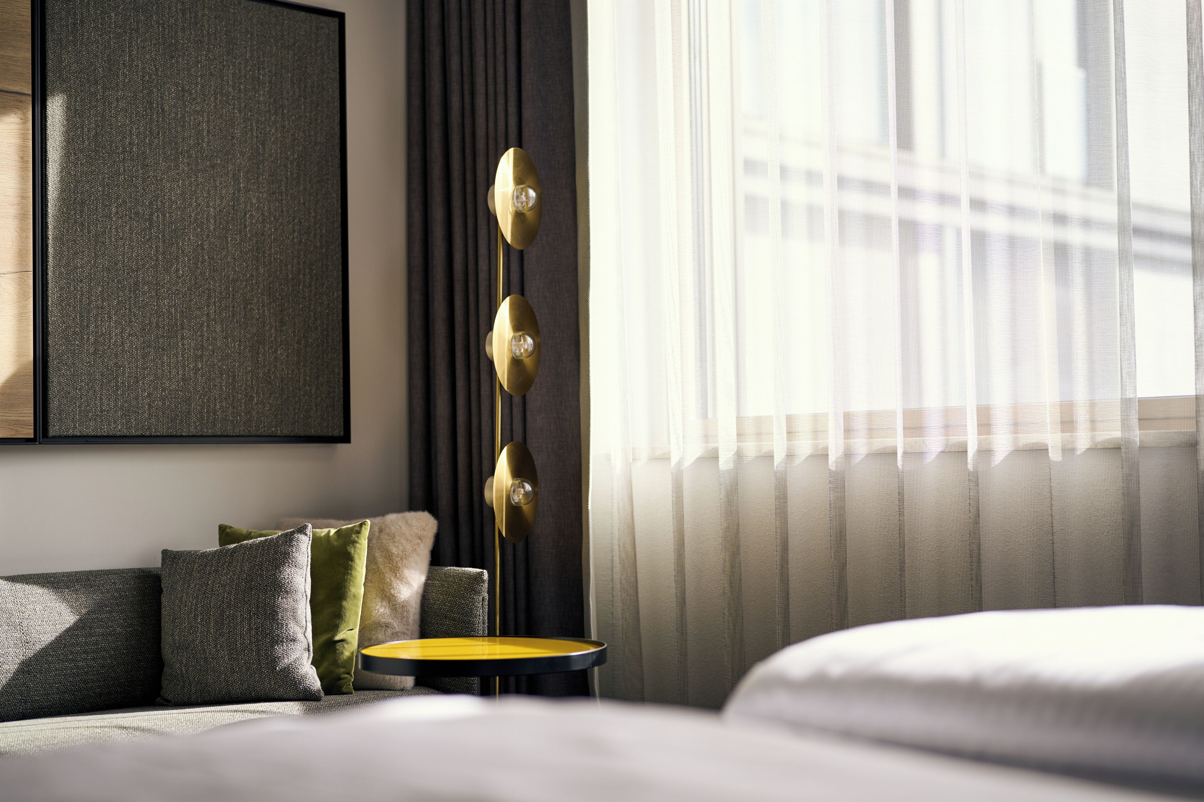 A modern hotel room with a bed, a small table, and a floor lamp.