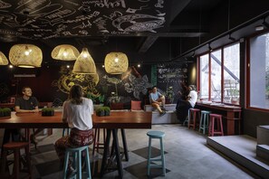 A modern cafe with wooden tables and stools, decorative wall art, and large windows. - Kitez Hotel & Bunkz - Hostel (Kuala Lumpur)