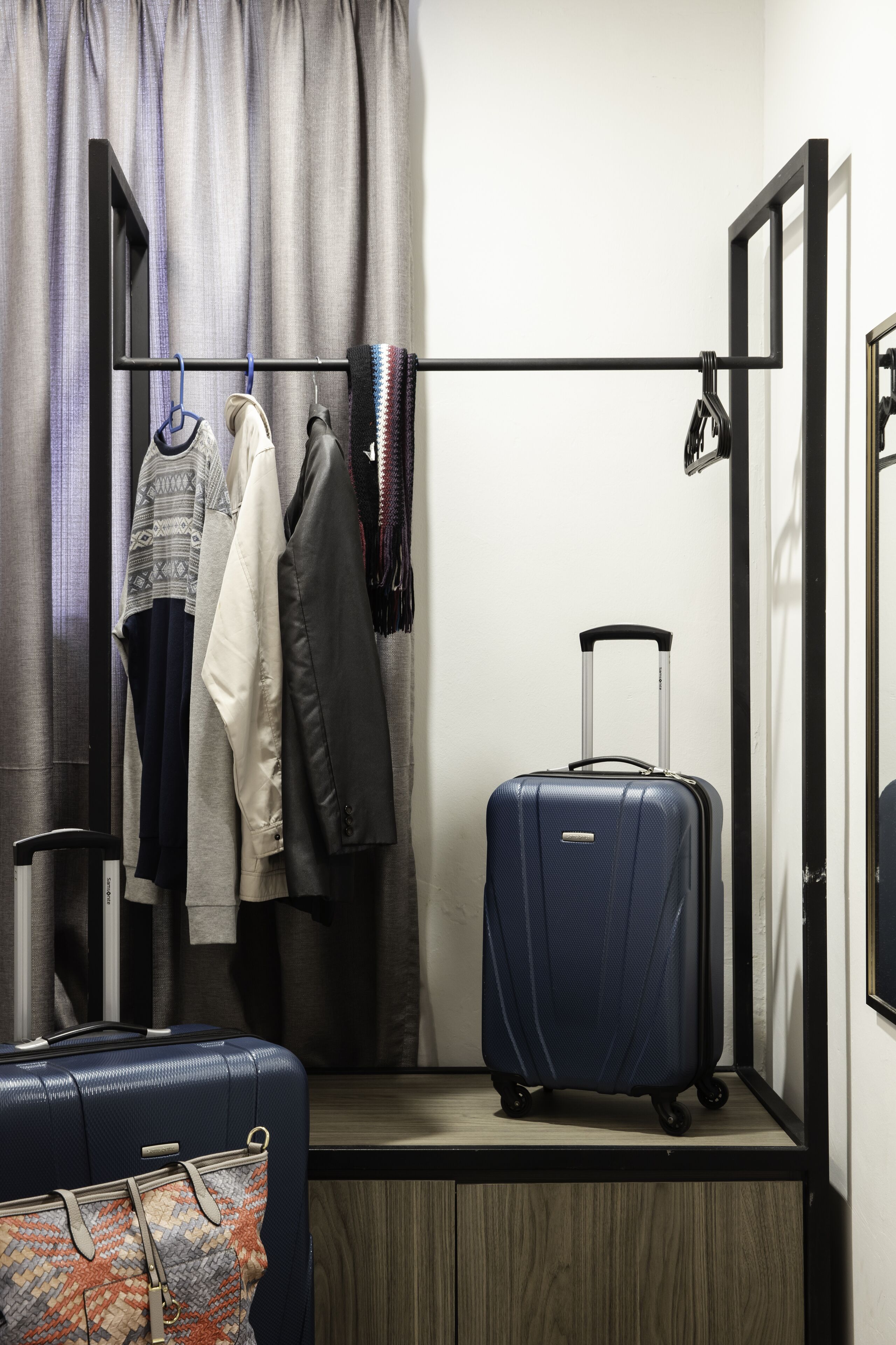 A hotel room with a bed, a wardrobe, a hanging rack with clothes, and a suitcase.