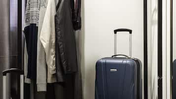 A hotel room with a bed, a wardrobe, a hanging rack with clothes, and a suitcase.