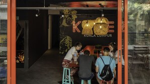 Een restaurant met glazen ingang, terras en een bord met de tekst 'KOKE KUALA LUMPUR'.