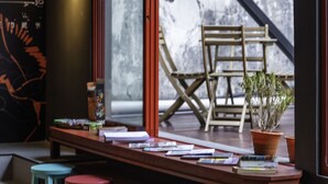 Een moderne bar met een houten toonbank, kleurrijke krukken en een groot raam met uitzicht op een terras.