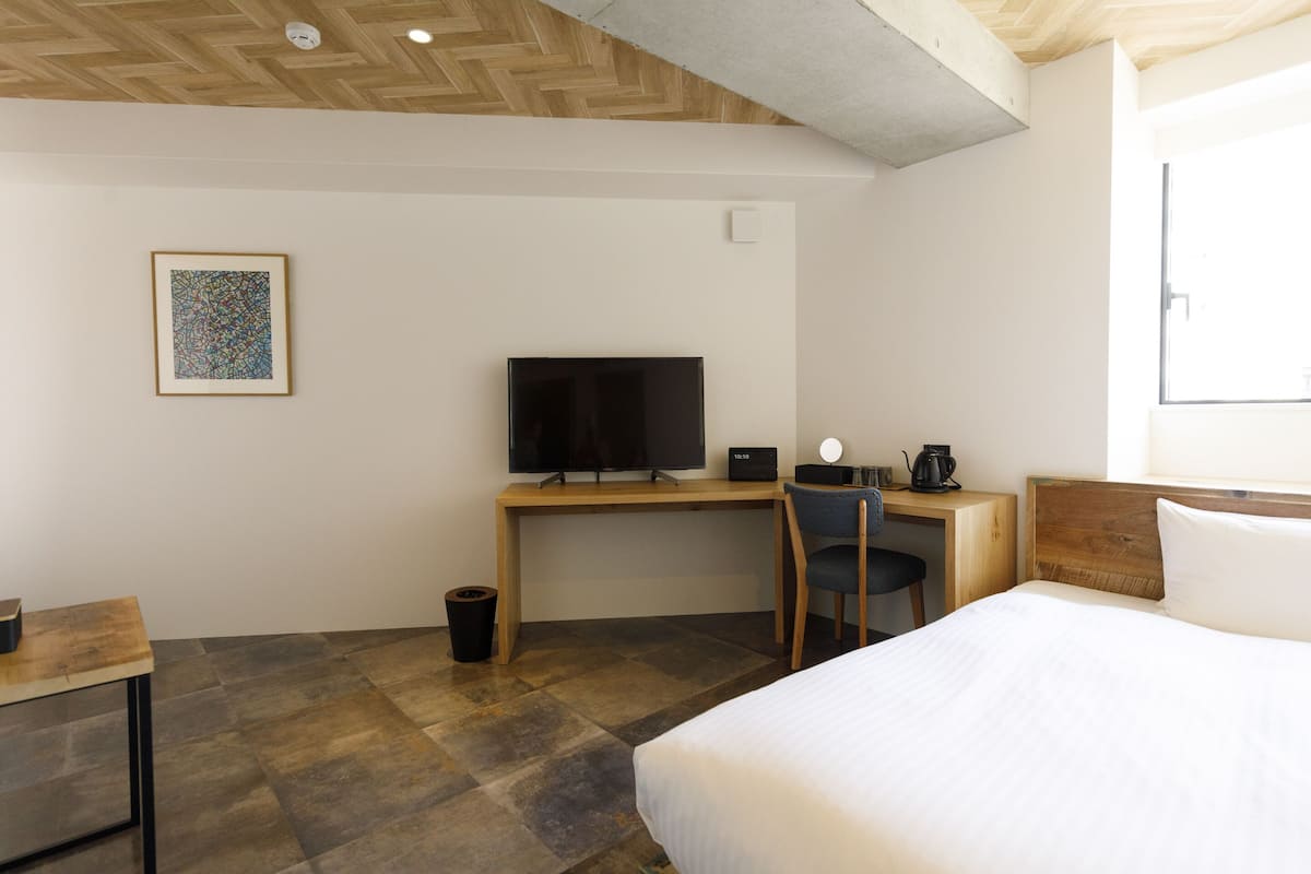 A hotel room with a bed, a desk with a TV, a chair, and a coffee machine.