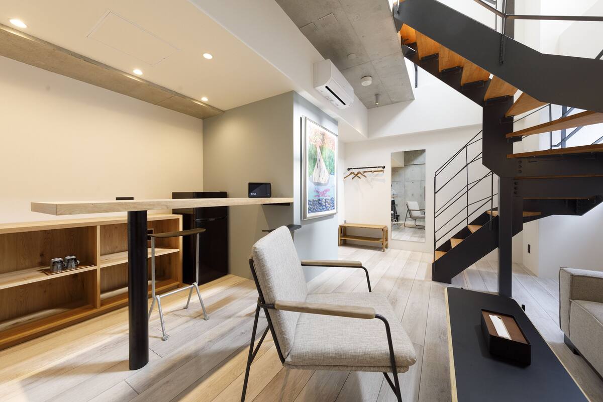 A modern interior with a wooden desk, a chair, a staircase, and a view of the outdoors.