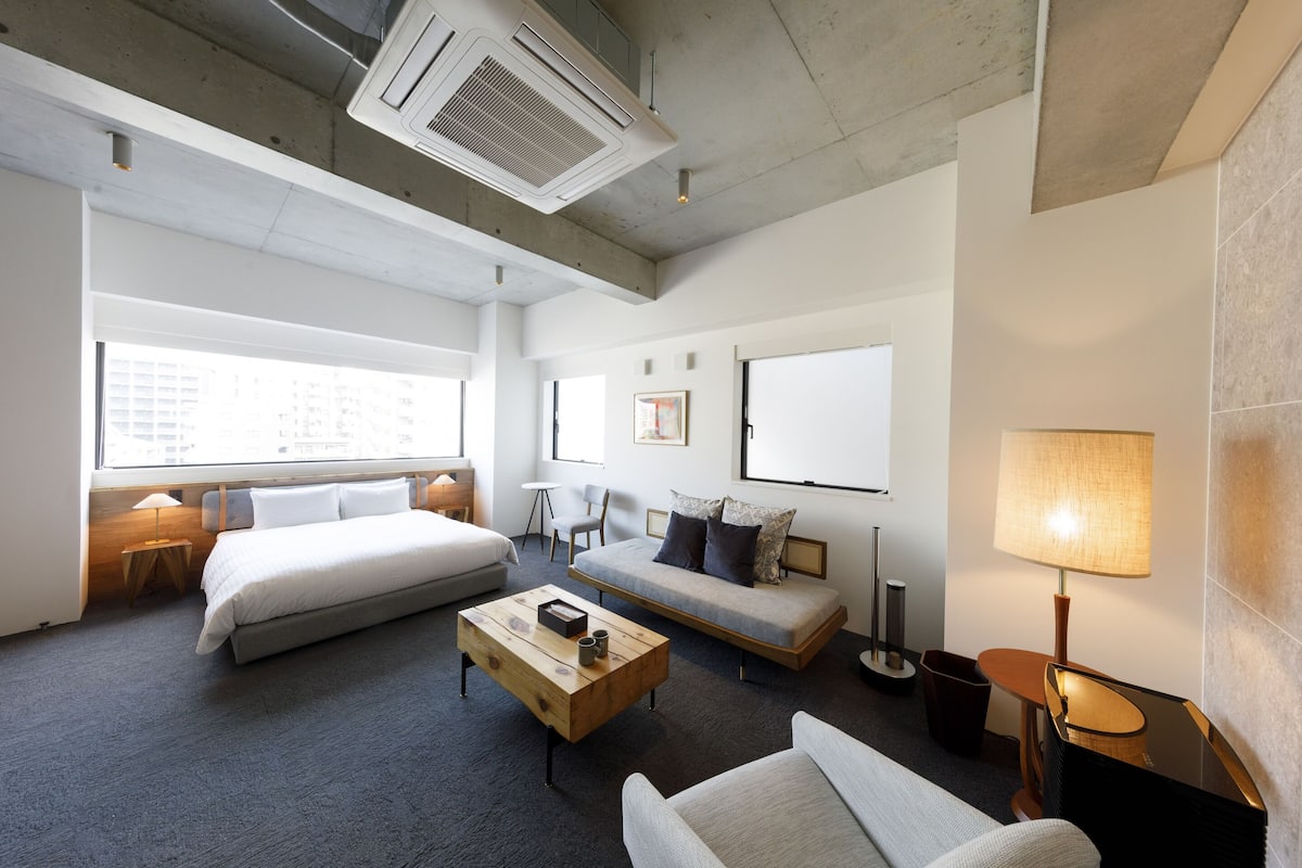 A hotel room with a large bed, a sofa, a coffee table, a desk, and a lamp.