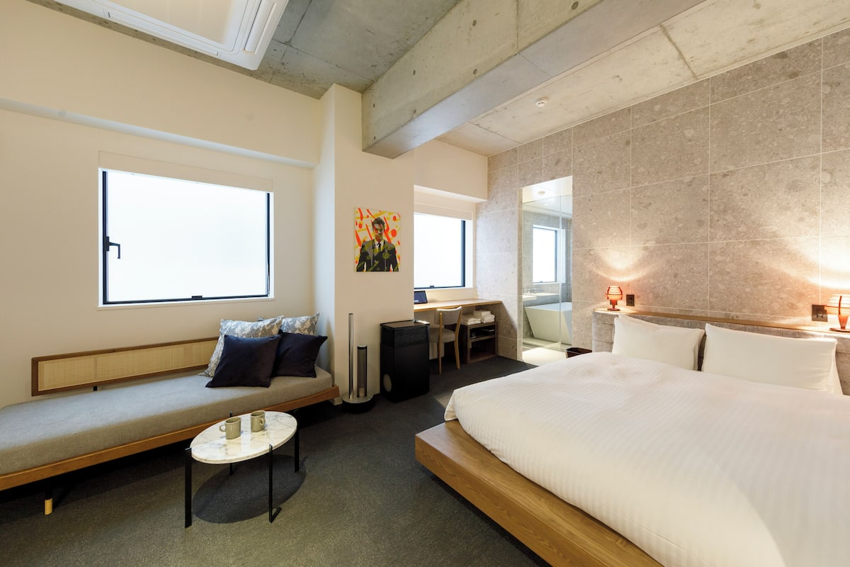 A modern hotel room with a large bed, a sofa, a small table, and a desk.