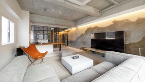 A modern living room with a sofa, a coffee table, and a TV. There is a kitchen area in the background with a bar and seating. - Hotel Mei Fukuoka Tenjin (Fukuoka)