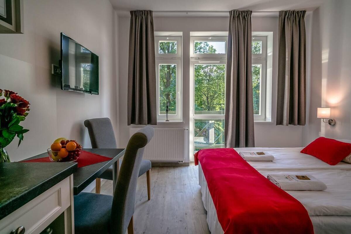 A hotel room with a bed, a desk with a chair, a TV mounted on the wall, and a window with curtains.