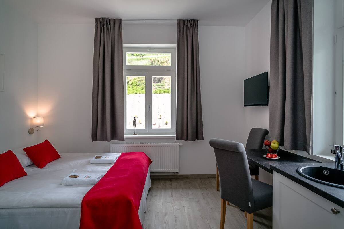 A hotel room with a bed, a desk, a chair, a TV, and a window with curtains.