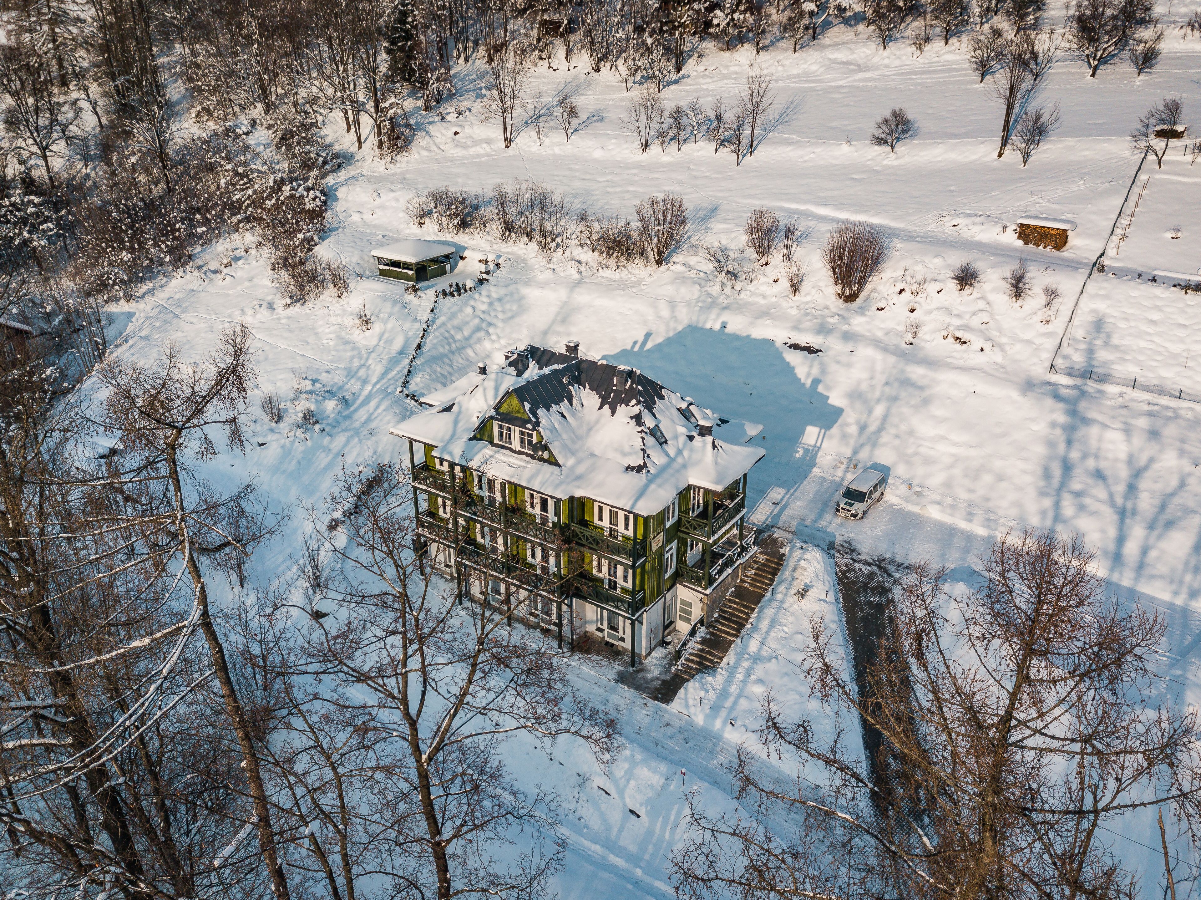 A multi-story house with a snow-covered roof, surrounded by trees and a snowy landscape.