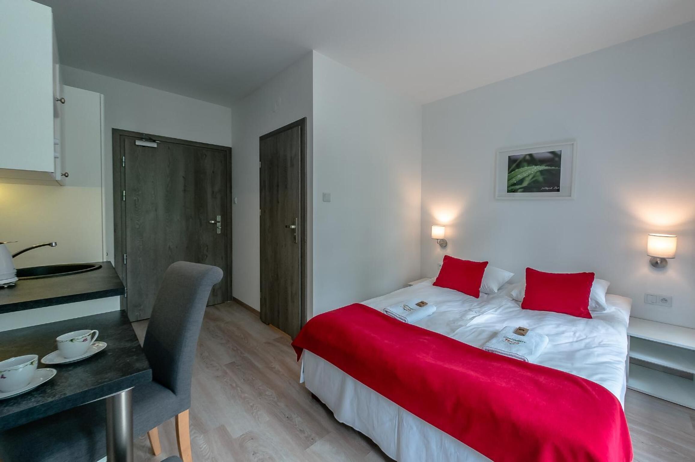 Una habitación de hotel moderna con cama, mesita de noche y una pequeña kitchenette.