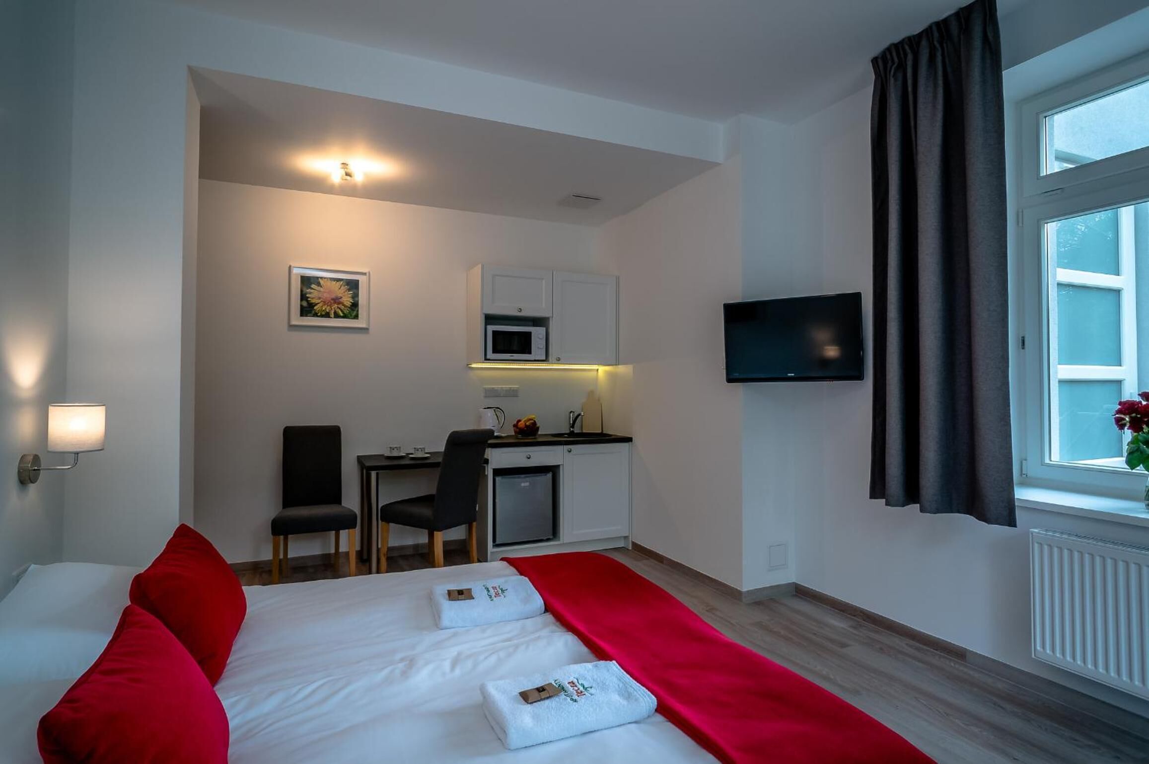 Hotellihuone, jossa on sänky, työpöytä tuolilla, mikroaaltouuni ja televisio.