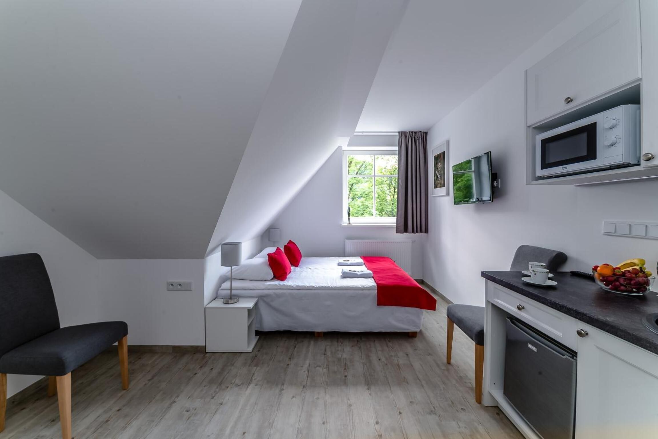 A modern, compact room with a bed, a desk, a microwave, and a small kitchenette.