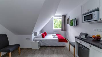 A modern, compact room with a bed, a desk, a microwave, and a small kitchenette.