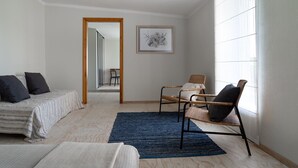 A bedroom with a bed, two chairs, a rug, and a framed picture on the wall.