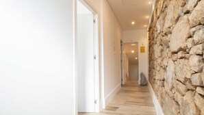 A hallway with a stone wall, wooden flooring, and white doors. - Elba Suites Gaia-Porto (Vila Nova de Gaia)