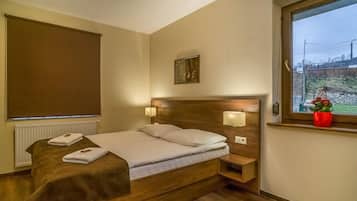 Una habitación de hotel con una cama de madera, un ventanal con vistas, un cuadro en la pared y una maceta roja.
