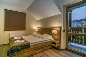 Um quarto com cama de madeira, mesa de cabeceira, luminária na parede e uma janela grande com vista para um edifício e árvores.