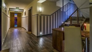 A hallway with wooden flooring, a staircase with striped railings, and a reception desk with a red candle.