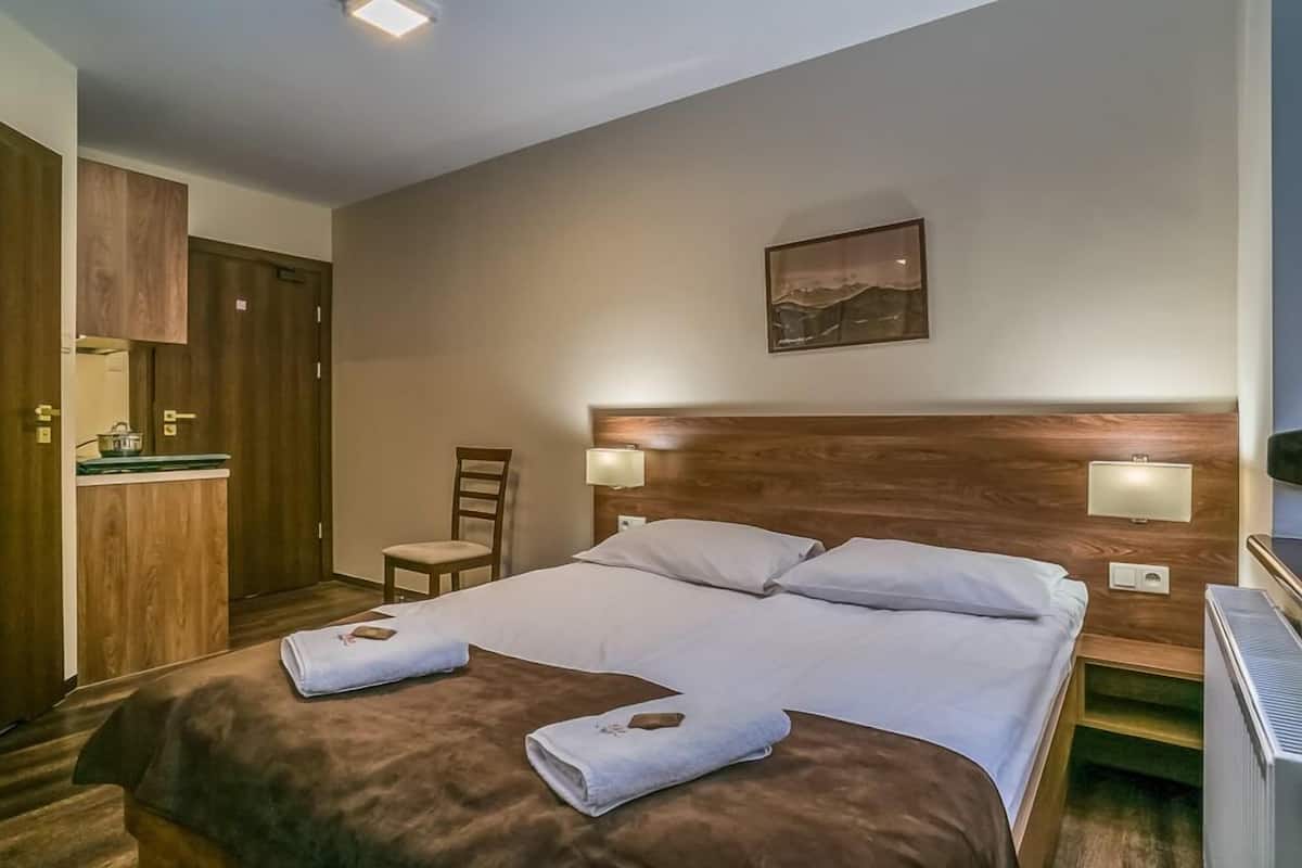 A hotel room with a wooden headboard, two beds, a desk with a chair, a small table, and a painting on the wall.