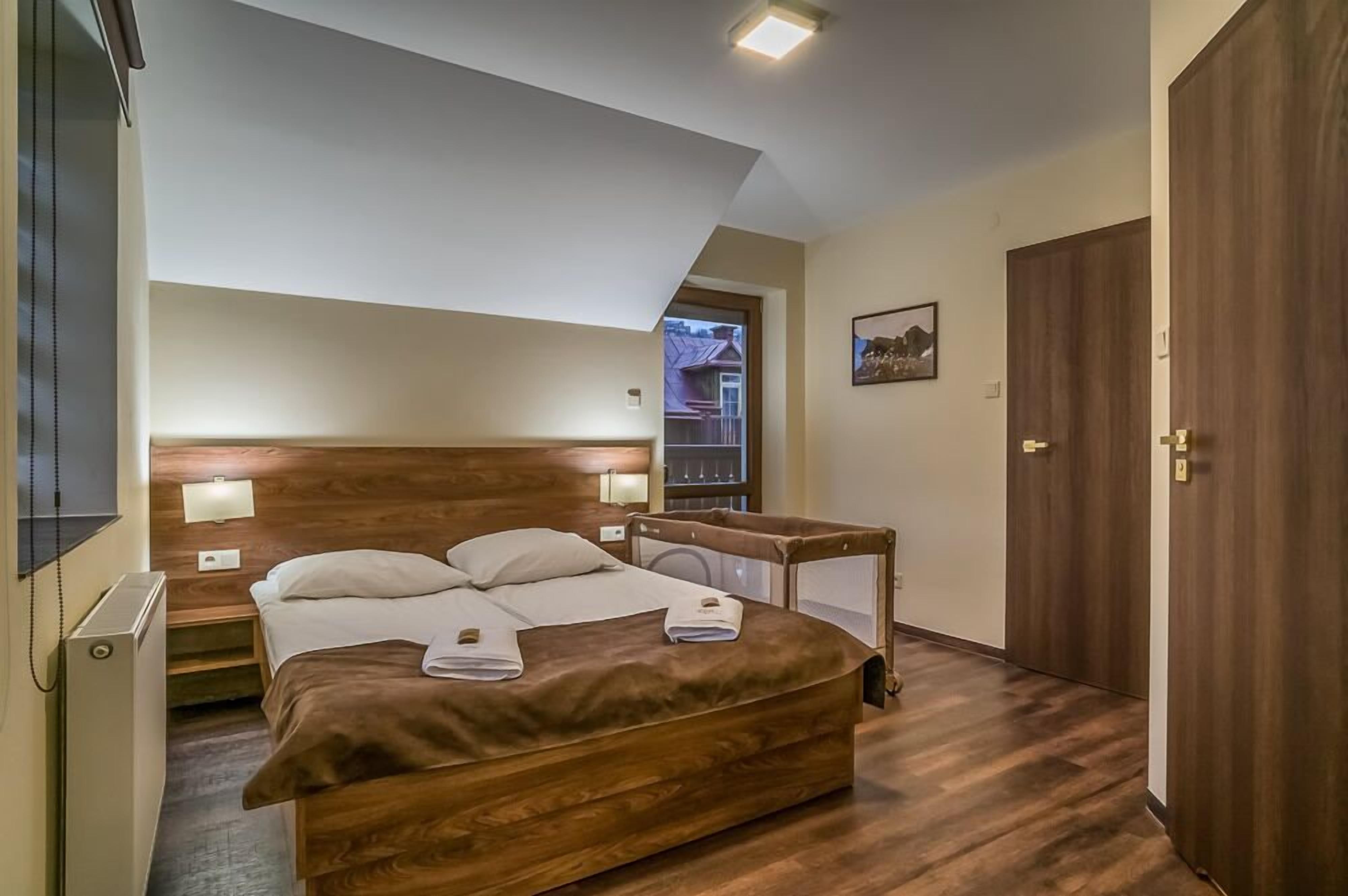 Une chambre avec un grand lit, une tête de lit en bois, des lampes de chevet et une vue sur l’extérieur.