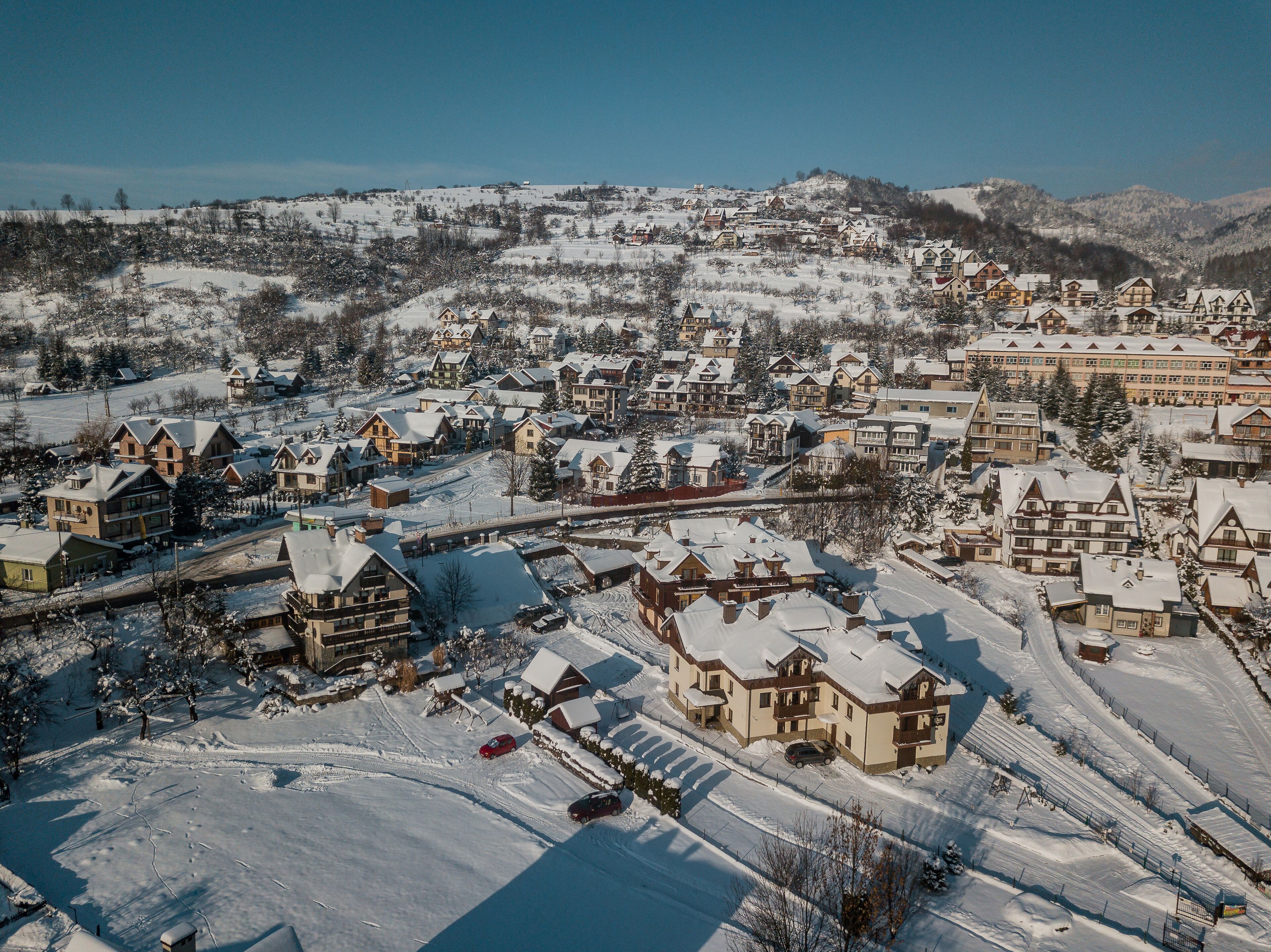 A snow-covered village with traditional chalet-style buildings, a main road, and a prominent hotel with a large building and multiple windows.